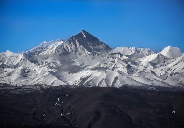 Stunning view of Mount Everest surrounded by snowy peaks under a clear blue sky.